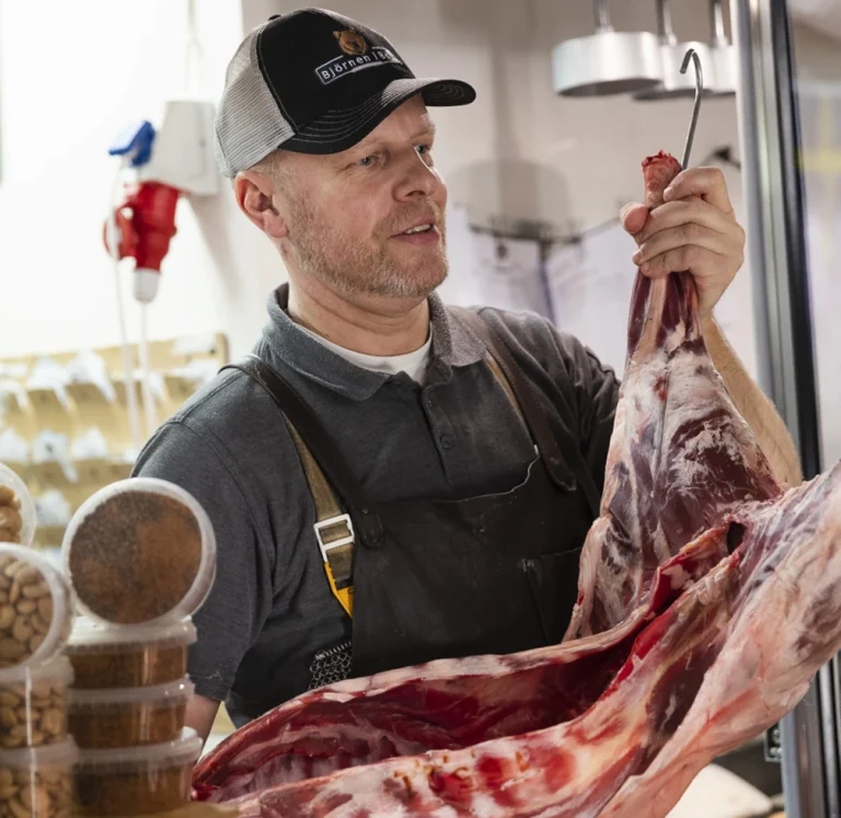 En slaktare hänger upp en hel lamn i sin delikatessbutik i Saltjö-Boo och Stockholm